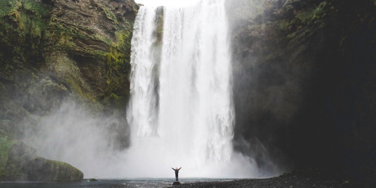 A huge waterfall in the background and a small figure standing at the bottom, raising their arms.